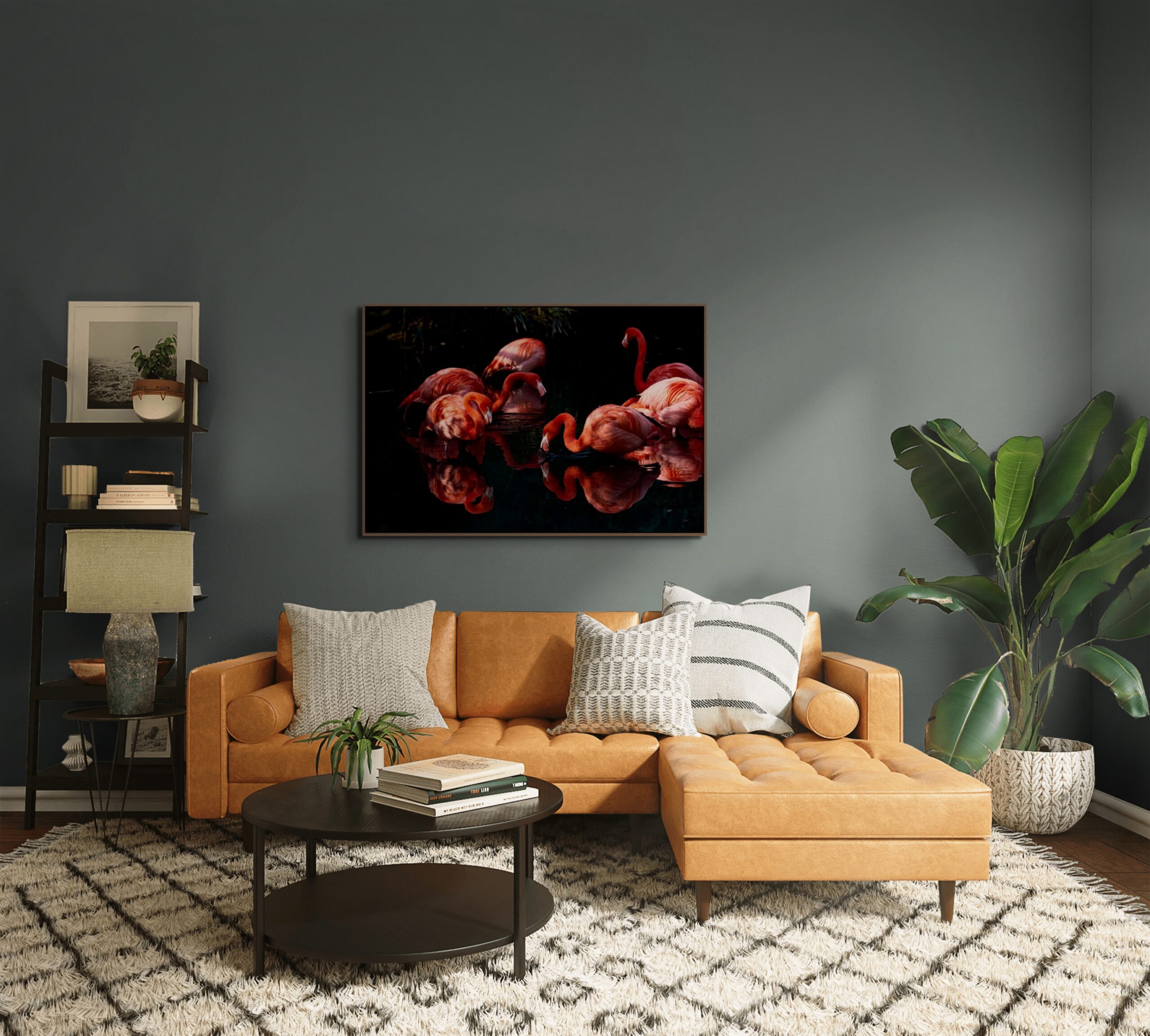 Mockup di un salotto moderno con pareti grigio scuro e divano in pelle color cuoio. Sopra il divano è esposta l'opera "Risonanze Simmetriche" di Antonio Milesi, che ritrae fenicotteri riflessi in uno specchio d'acqua scuro in stile pittorialista. Mockup of a modern living room with dark gray walls and a tan leather sofa. Above the sofa hangs the artwork "Symmetric Resonances" by Antonio Milesi, depicting flamingos reflected in dark water in a pictorialist style.